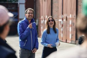 A man and a woman are talking to a group facing them.